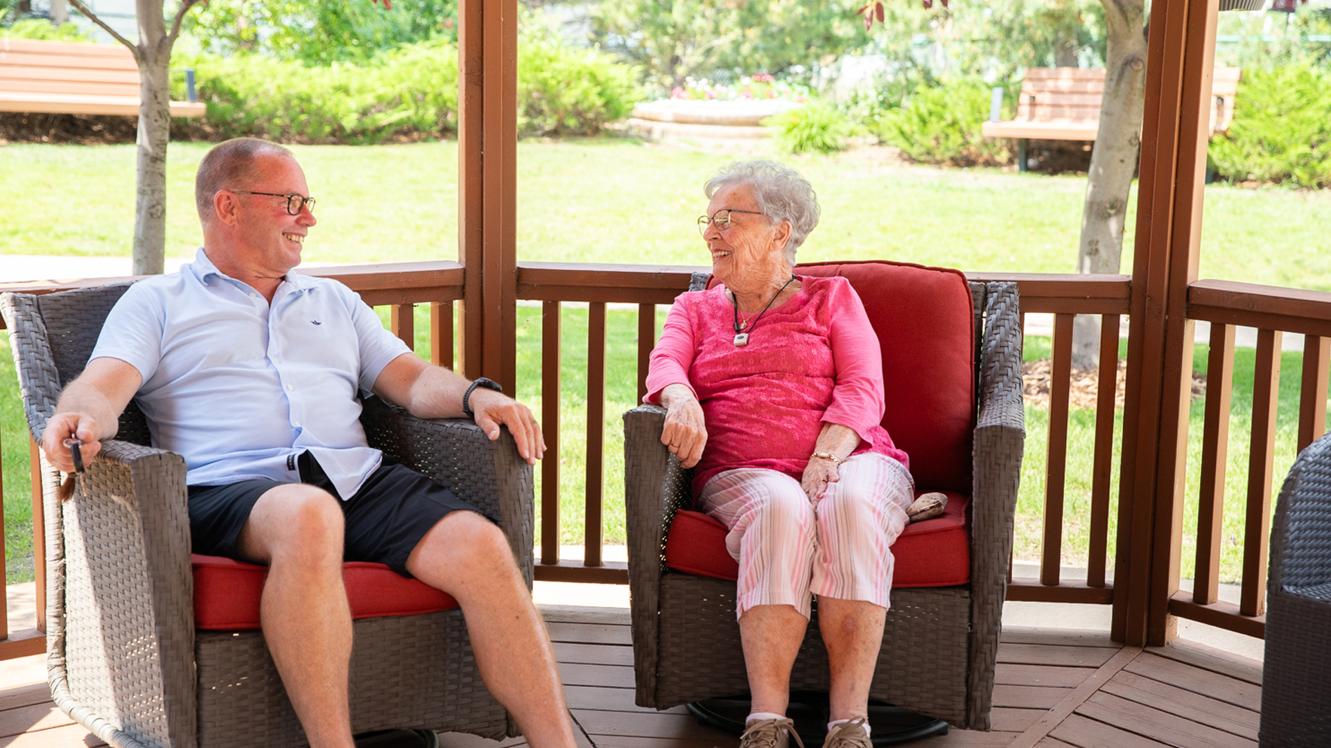 Senior seated with a loved one outdoors. Both people are smiling.