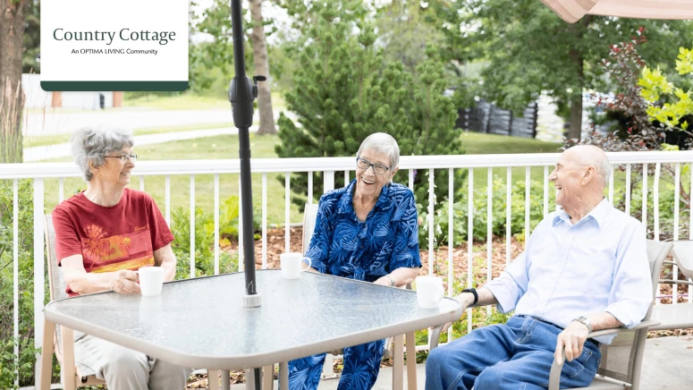 A group of three seniors sitting at an outdoor patio table drinking coffee