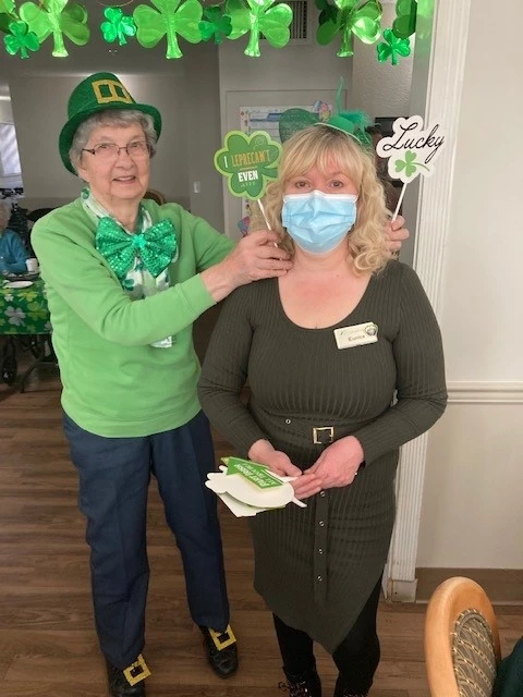 A senior posing with a staff member while holding a bunch of St. Patrick's Day signs
