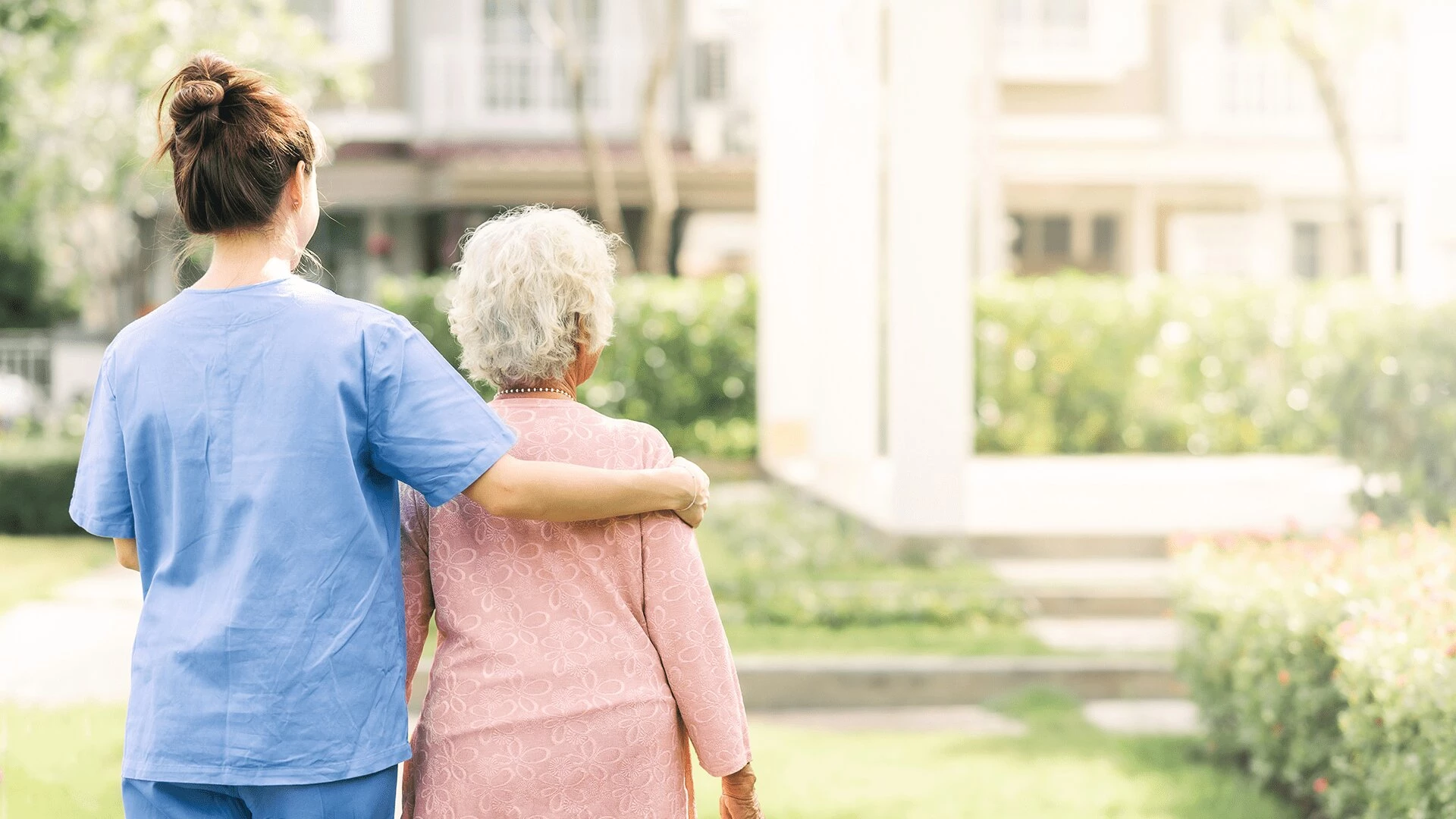 An elderly woman walking with nurse in garden at a senior home