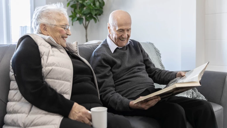 An elderly couple smiling while reading a book and having coffee