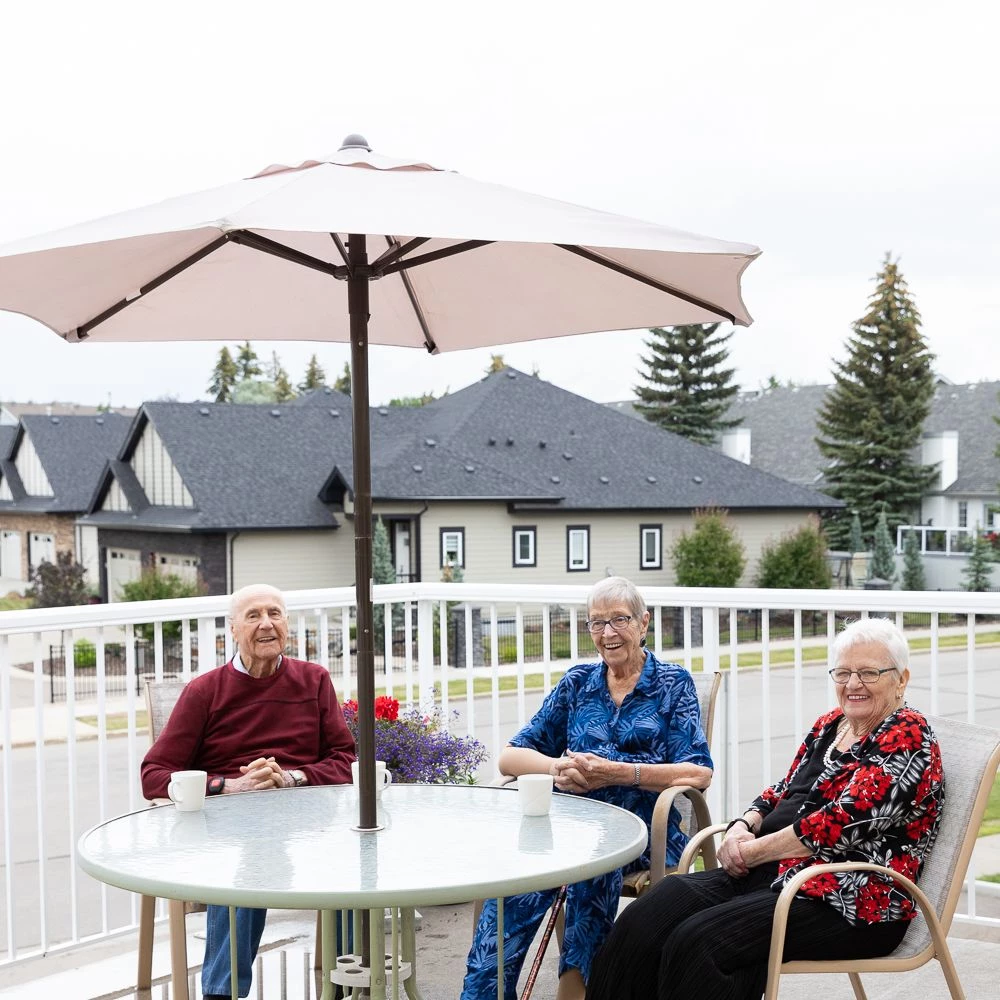 Three seniors seated together on the outdoor patio space. They are smiling together.